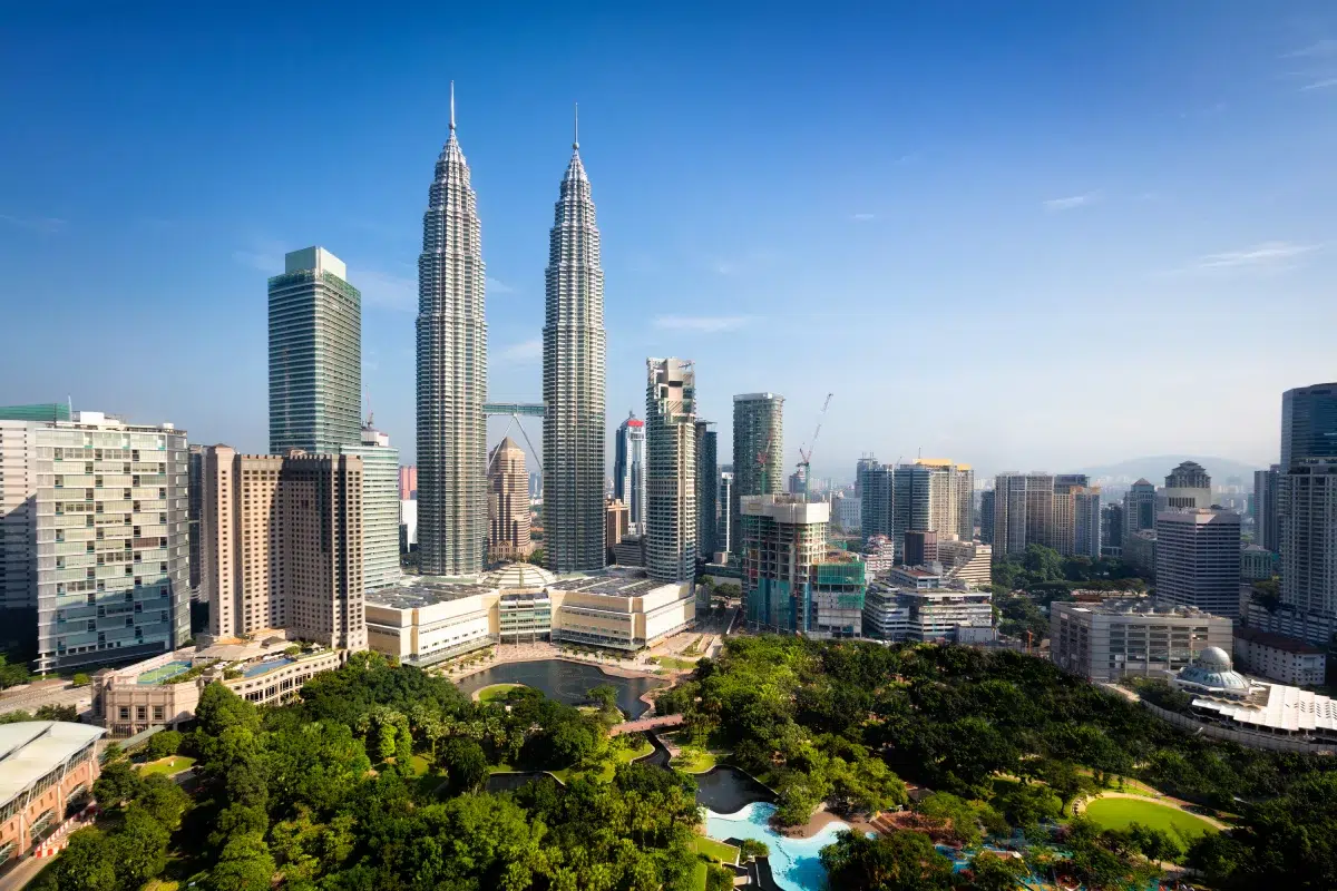 A panoramic view of Kuala Lumpur city center featuring the iconic Petronas Twin Towers, lush KLCC Park, and nearby skyscrapers — ideal scene for a 쿠알라룸푸르 호텔 stay.
