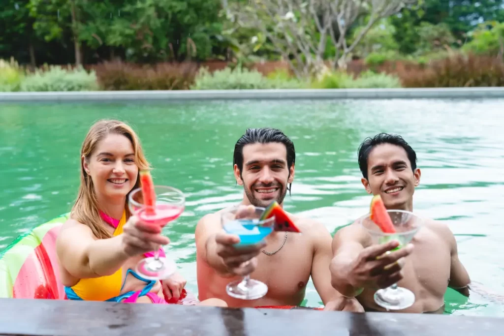 Group of friends showing their cocktails at a pool at their hotel staycation in Singapore